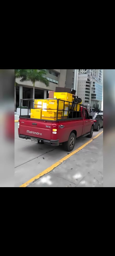 Camioneta pickup roja Mahindra cargada con cajas amarillas estacionada en calle urbana