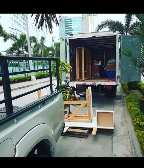 Camión de mudanza cargado con muebles de madera y cajas estacionado en calle de ciudad con palmeras y edificios